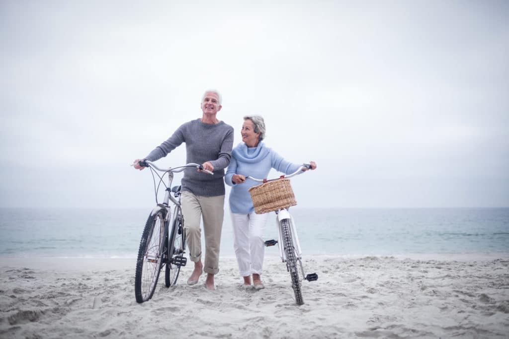 Couple Walking With Bikes on the Beach for Cardio Exercise - Medicare Plan Finder